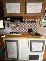 Modernized RV rental kitchen: gray cabinets with patterned panels, patterned backsplash, wood counter, sink & stove.