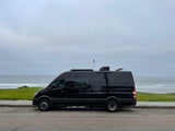 A black camper van RV rental is parked by the ocean on an overcast day, ready for adventure.