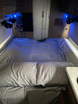 Cozy RV rental bedroom featuring a made bed with grey sheets, blue accent lighting, and wall-mounted control panels.