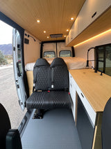 Inside a chic rv rental camper van: quilted black seats, wooden ceiling, kitchen, comfortable bed, and scenic views.