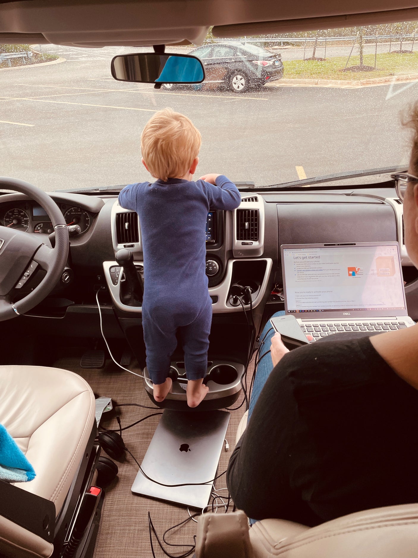 Rainy day inside an RV rental: a curious child stands at the dash, while an adult works on a phone activation.