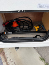 RV rental storage with a coiled power cord, e2 hitch bar, and Reese coupler lock for secure towing and hookup.