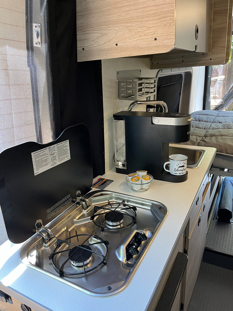 Compact kitchenette in an RV rental, featuring a stove, sink, and coffee maker. Perfect for road trip cooking and coffee! — photo 10