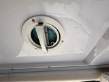 Inside an RV rental: Circular light fixture/vent on a glossy white ceiling, showing reflections and a curtain rail.