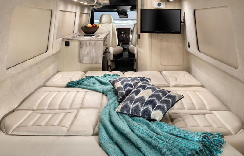 Enjoy this spacious RV rental camper van with a cozy bed, plush blanket, and a scenic beach view through the front. — photo 5