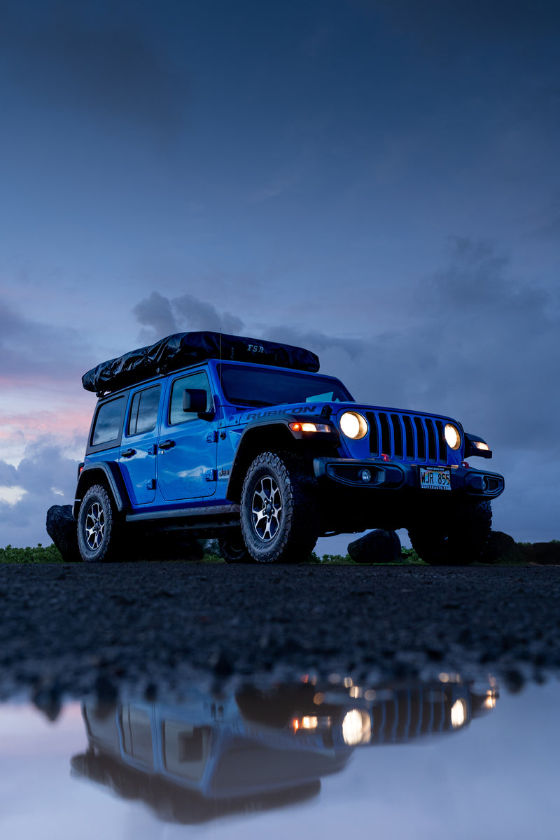 Blue Jeep Rubicon with glowing headlights and rooftop tent at dusk, reflected in a puddle. Ideal for a rugged rv rental adventure! — photo 3