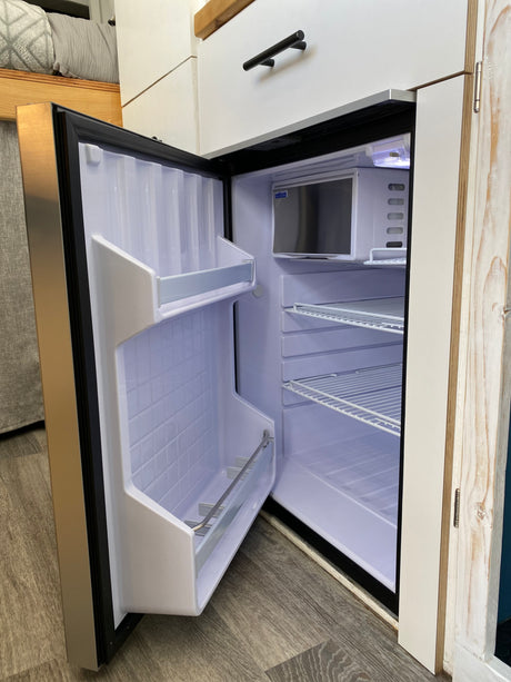 This RV rental features an open, clean compact refrigerator with interior shelves, perfect for your journey.