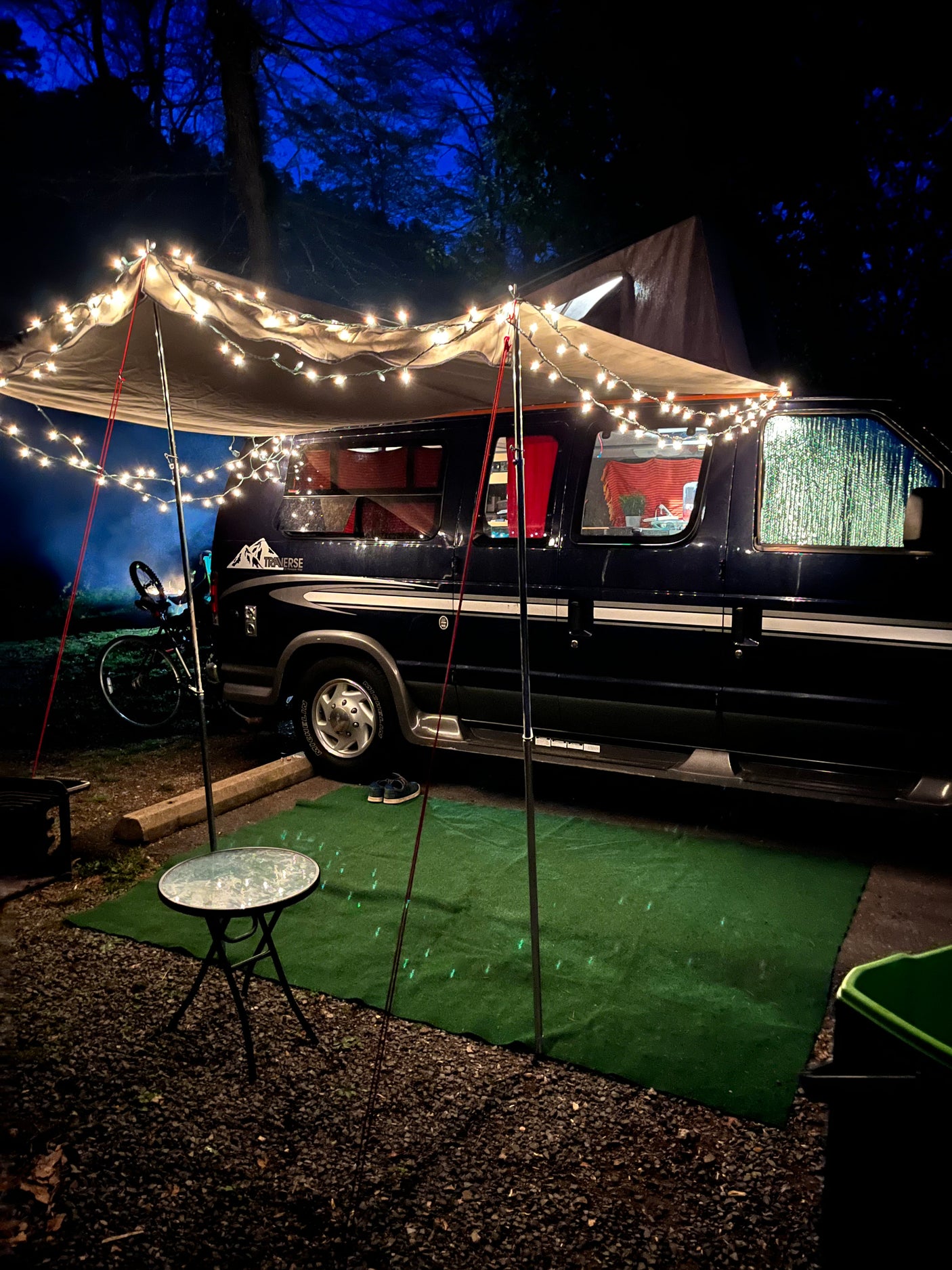 Cozy night setup: an RV rental campervan with a lighted awning, bike, and table, creating a welcoming camp scene.
