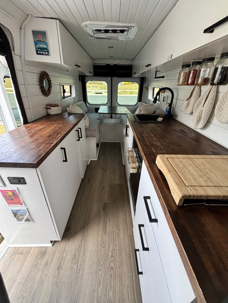 This RV rental features a modern white interior with dark wood countertops, a full kitchenette, rear dining area, and light wood flooring.