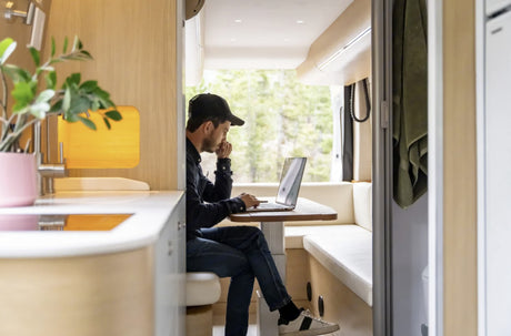Man works on laptop in a stylish RV rental, featuring light wood interior and nature views. Ideal for remote work.