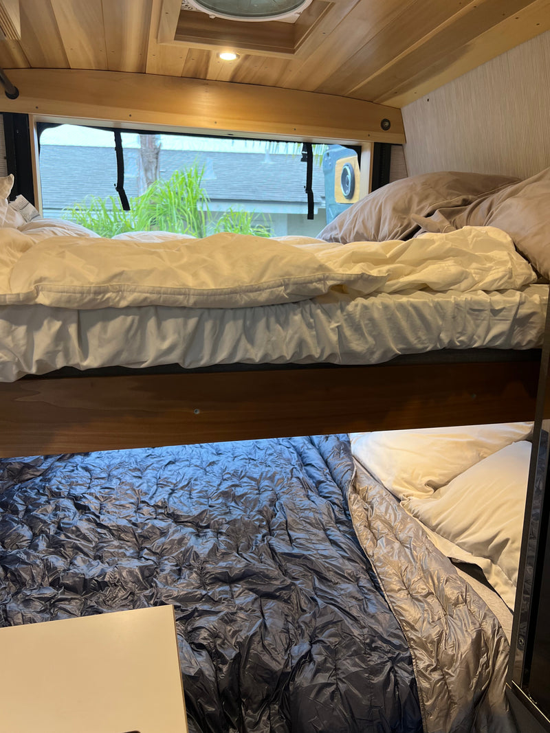Inside an RV rental, a cozy bunk bed setup. The top bunk has white bedding, and the lower bunk features a shiny gray sleeping bag. — photo 15