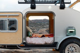 RV rental comfort: A teardrop trailer's open door reveals a cozy bed & stunning desert vista, powered for off-grid adventures.