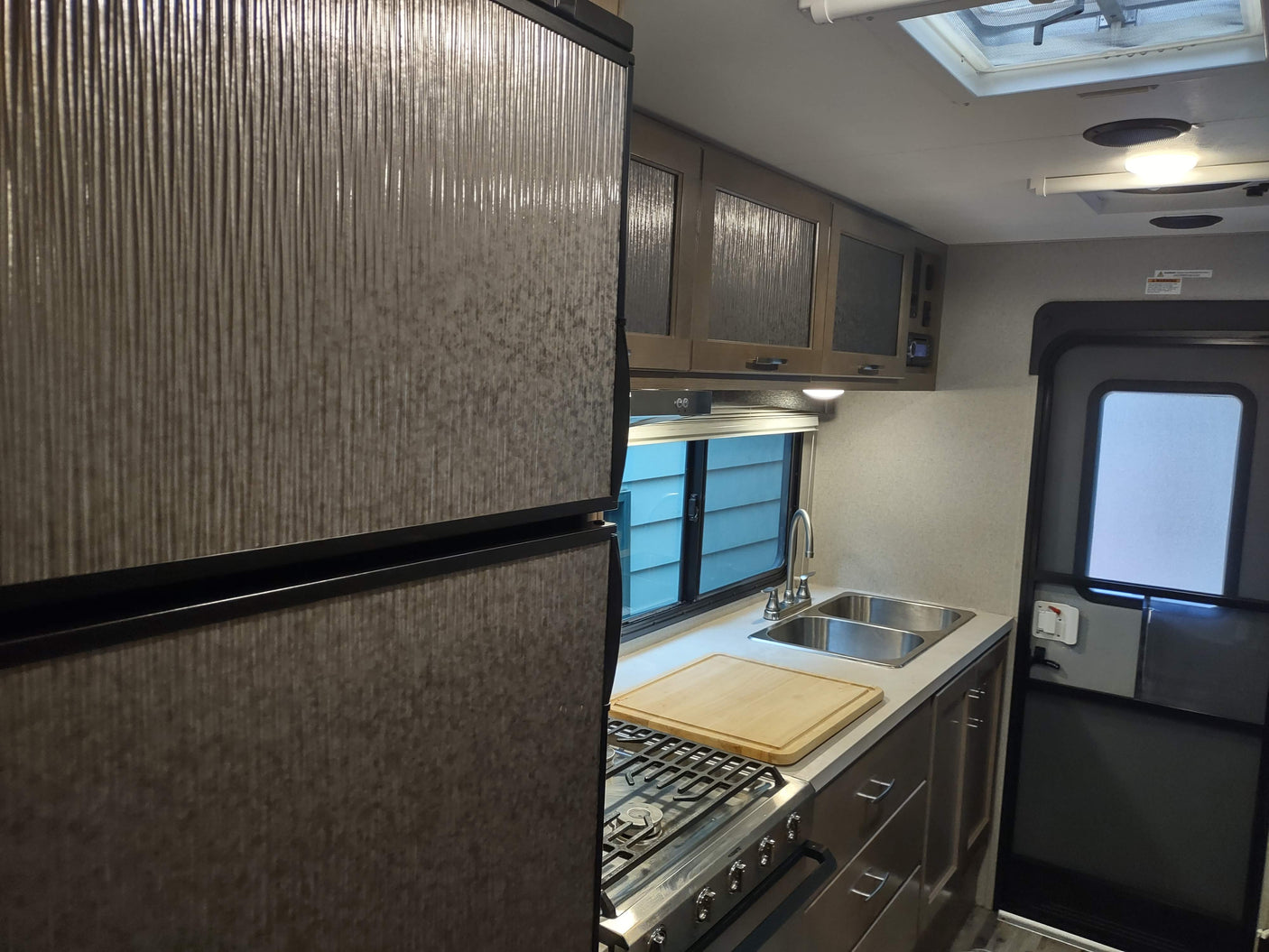 Compact RV rental kitchen interior: stainless steel appliances, dual sink, patterned fridge & cabinets. Ready for travel.