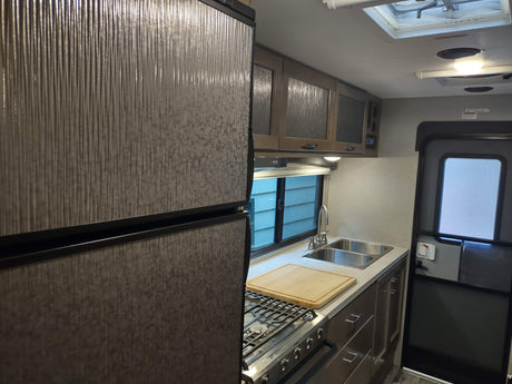 Compact RV rental kitchen interior: stainless steel appliances, dual sink, patterned fridge & cabinets. Ready for travel.