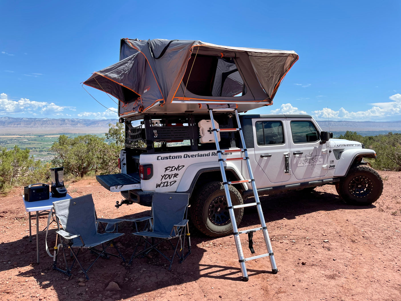 Custom RV rental Jeep Gladiator with rooftop tent ready for overlanding, set up for camping at a scenic overlook.