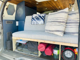 RV rental: View of a camper van's comfortable gray bench seat, built-in storage with camping gear, and wood-paneled ceiling.