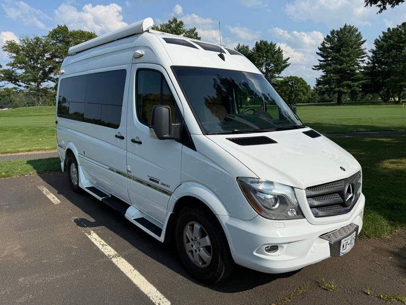  parked on asphalt with trees & sky in the background.|White Mercedes-Benz Sprinter rv rental van parked on asphalt. A green golf course & trees are visible under a blue sky.|White Mercedes-Benz Sprinter rv rental van. Front view — photo 7