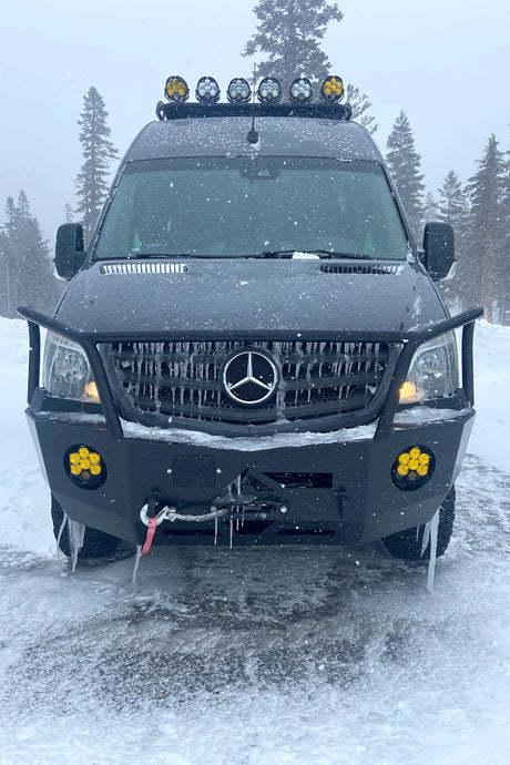 Front view of a black Mercedes Sprinter RV rental, covered in snow and icicles, ready for rugged winter adventures.