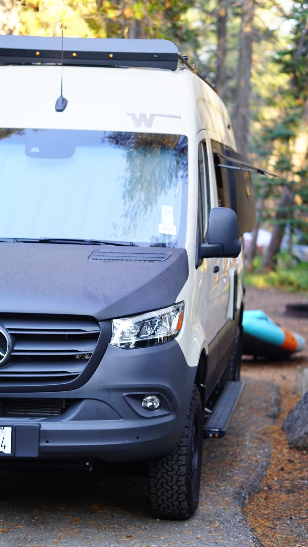  ready for adventure.|A child sits by a cream-colored Revel 4x4 camper van in a sunny forest — photo 3