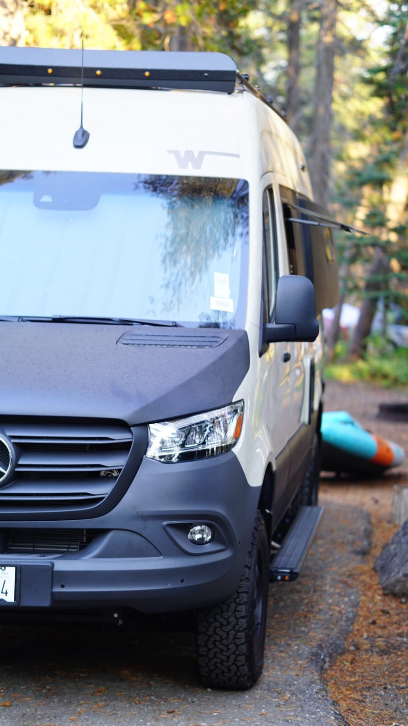  ready for adventure.|A child sits by a cream-colored Revel 4x4 camper van in a sunny forest — photo 3