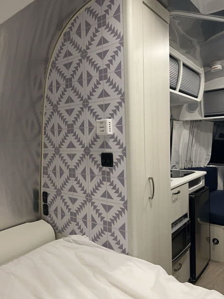 Cozy rv rental interior: patterned wall, bed, and kitchenette with microwave & fridge. Ideal camper setup.
