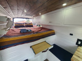 This cozy RV rental features a comfy bed with striped bedding, wood ceiling, and smart storage solutions for your travels.