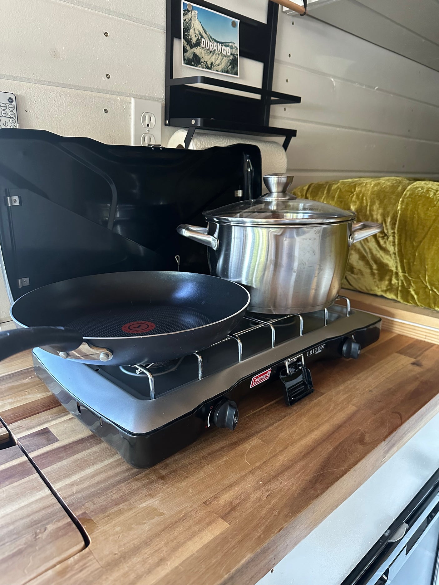 RV rental cooking: A Coleman portable stove with a frying pan and pot on a warm wood countertop.
