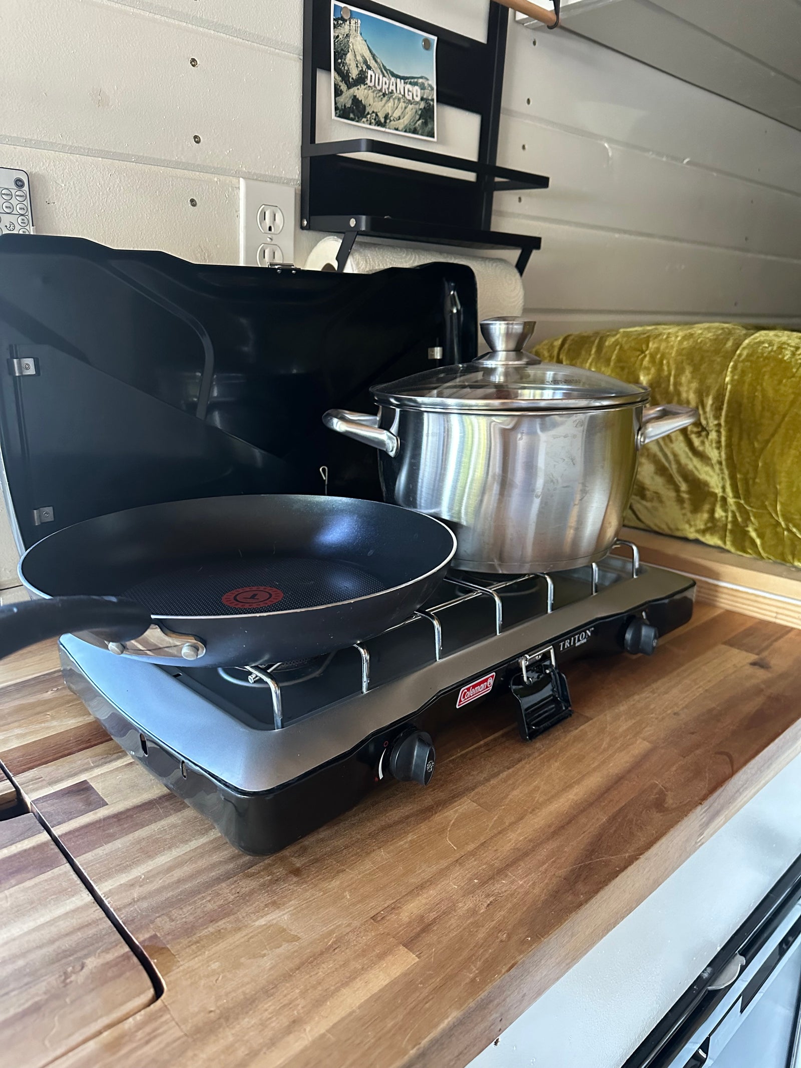 RV rental cooking: A Coleman portable stove with a frying pan and pot on a warm wood countertop.