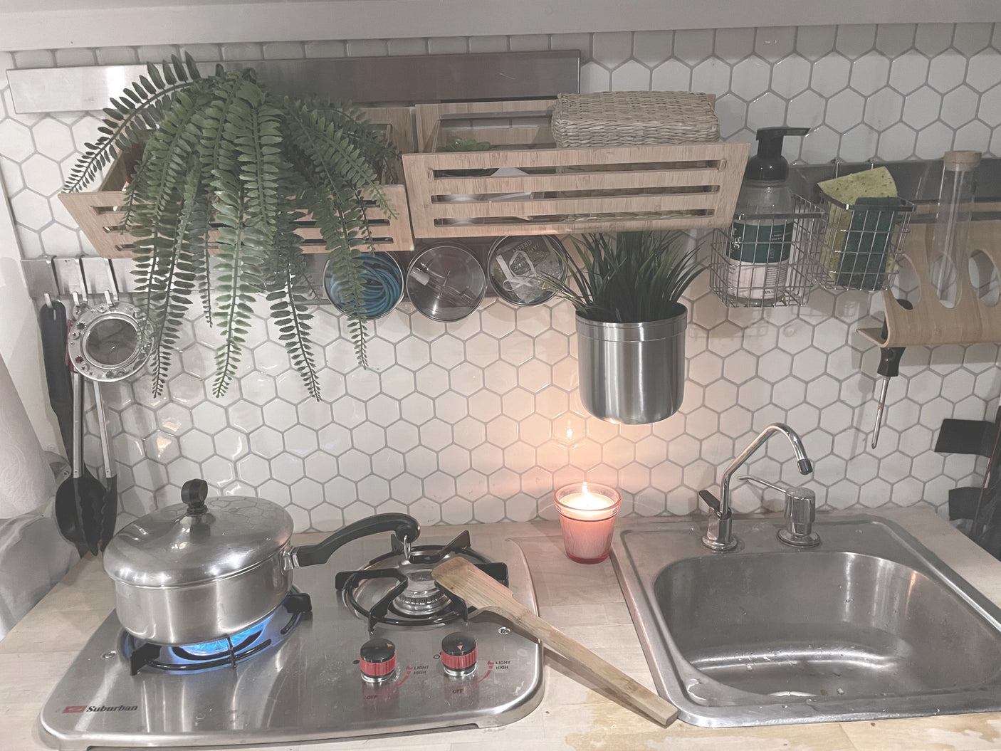 A cozy, organized RV rental kitchen with a lit portable stove, sink, and various wall-mounted items, ideal for compact travel.