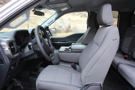 Inside a gray pickup truck, showing fabric seats, steering wheel, and console with cupholders, suitable for an RV rental adventure.