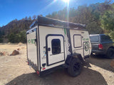 Explore nature with an RV rental! White off-road camper trailer & truck parked by sunny rocky cliffs for camping.