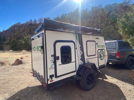 Explore nature with an RV rental! White off-road camper trailer & truck parked by sunny rocky cliffs for camping.