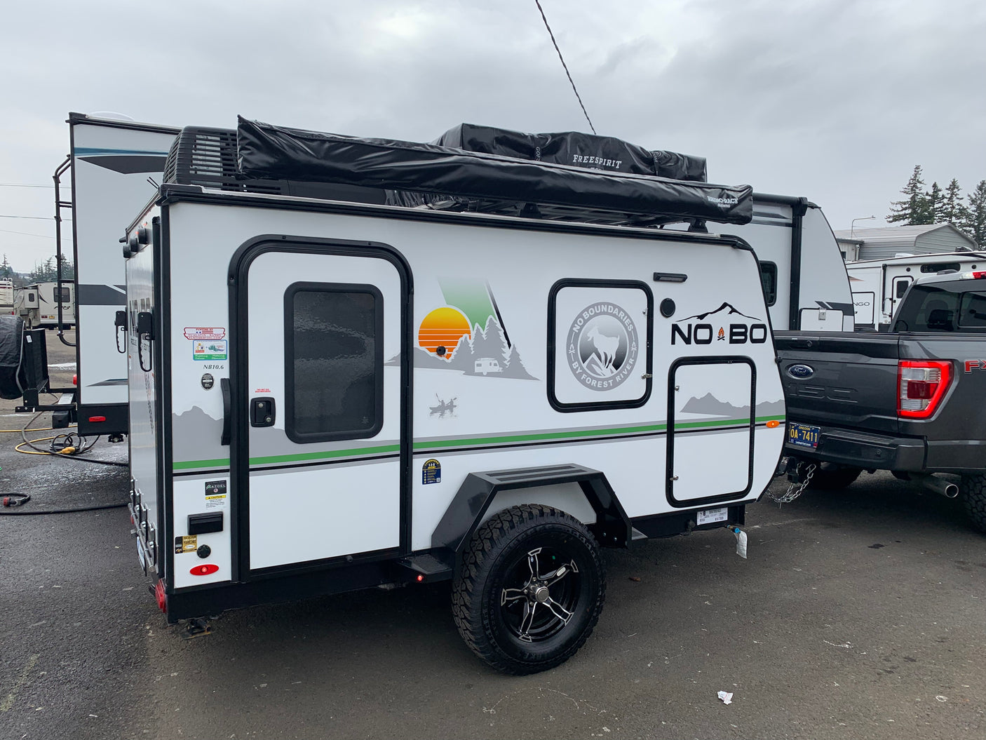 White & gray No Boundaries RV rental, a compact off-road travel trailer, shown hitched to a dark pickup truck.