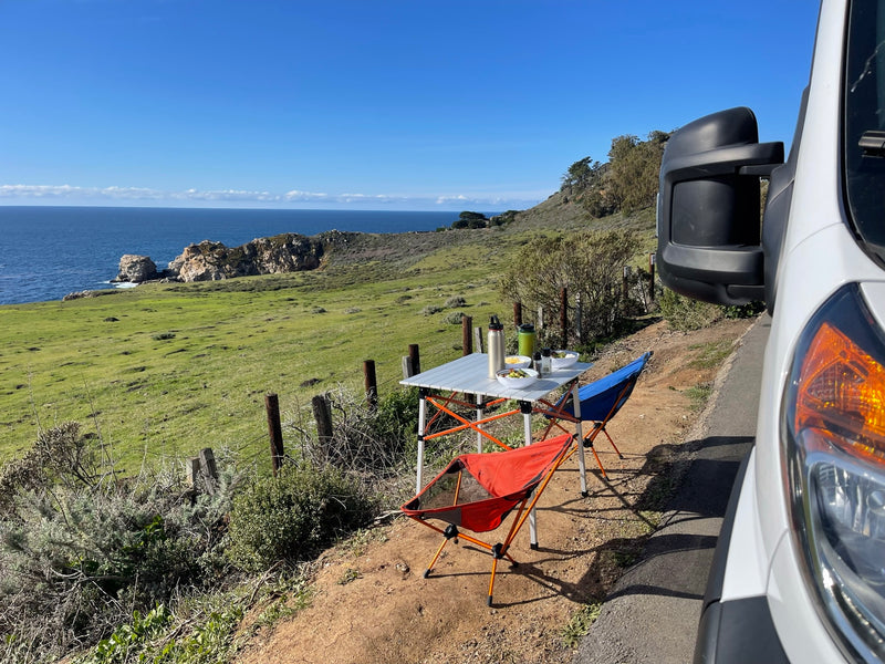  offering a stunning ocean view over green coastal hills.|White Winnebago Solis RV rental parked at a dark campsite with other RVs — photo 7
