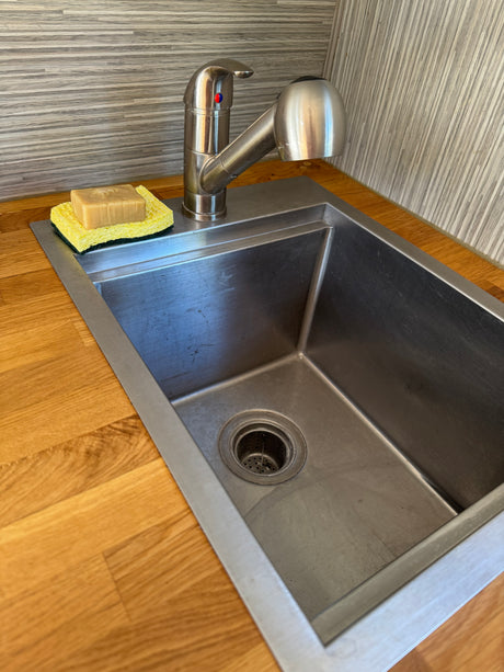 Compact stainless steel sink and pull-down faucet in an RV rental kitchen, with soap and sponge on a wooden counter.