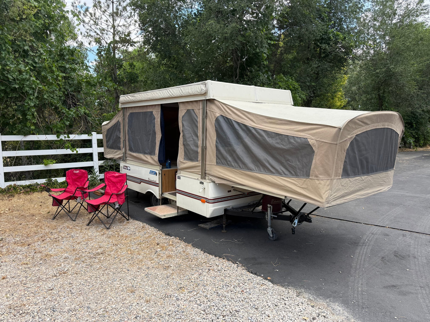  ready for camping in a wooded outdoor setting.|Coleman pop-up RV rental fully set up with red camping chairs