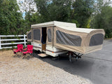  ready for camping in a wooded outdoor setting.|Coleman pop-up RV rental fully set up with red camping chairs