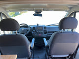 RV rental cockpit view from passenger area, showing front seats, dashboard with steering wheel, and road through windshield.