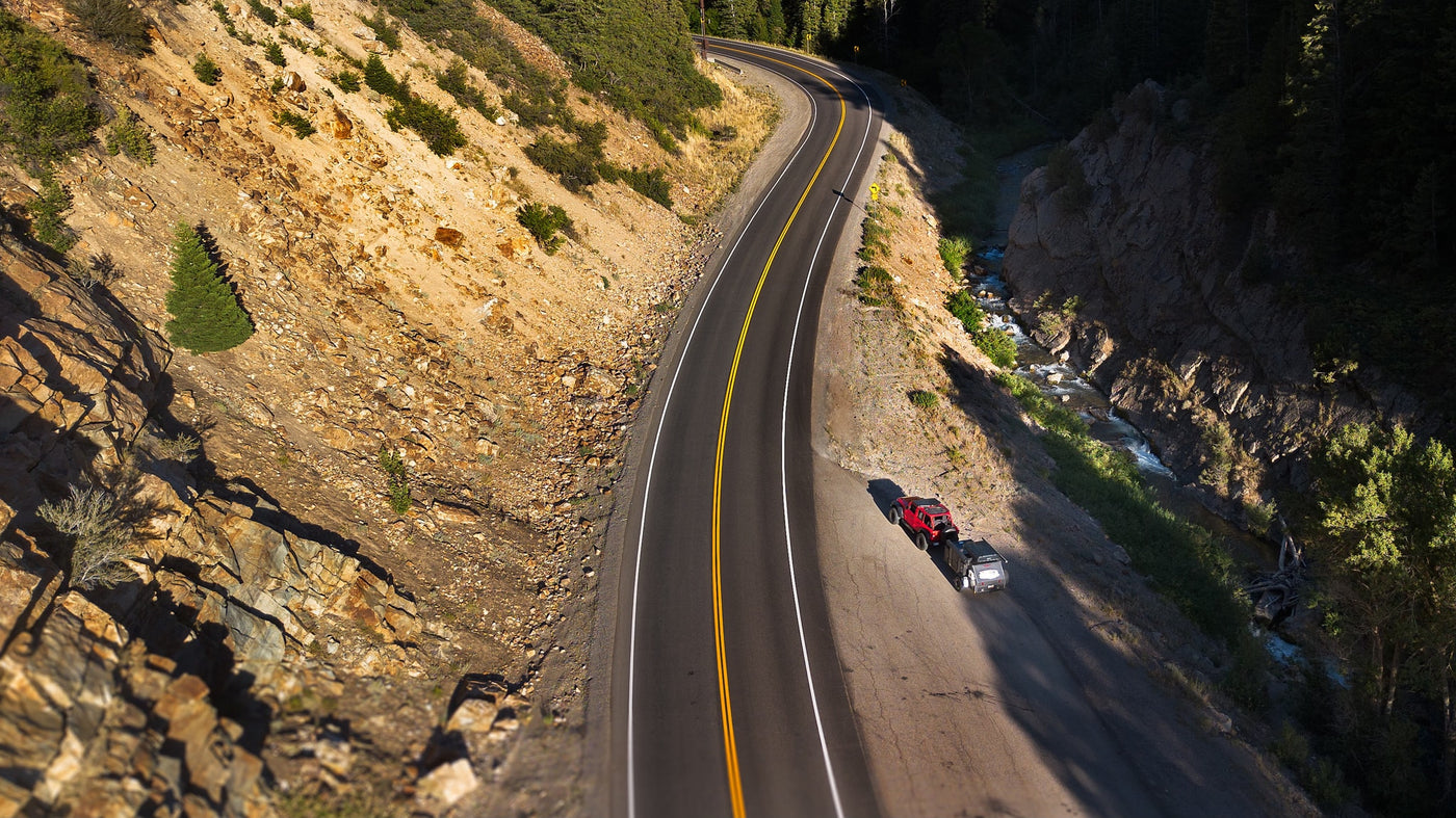 Overhead view of a red truck and a compact rv rental camper parked on a scenic mountain road beside a river. — photo 15
