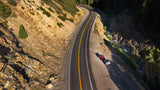 Overhead view of a red truck and a compact rv rental camper parked on a scenic mountain road beside a river.