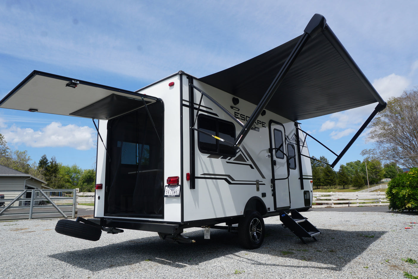 This white RV rental, an Escape model, showcases its extended awning, open rear hatch with screen, and deployed steps for camping.