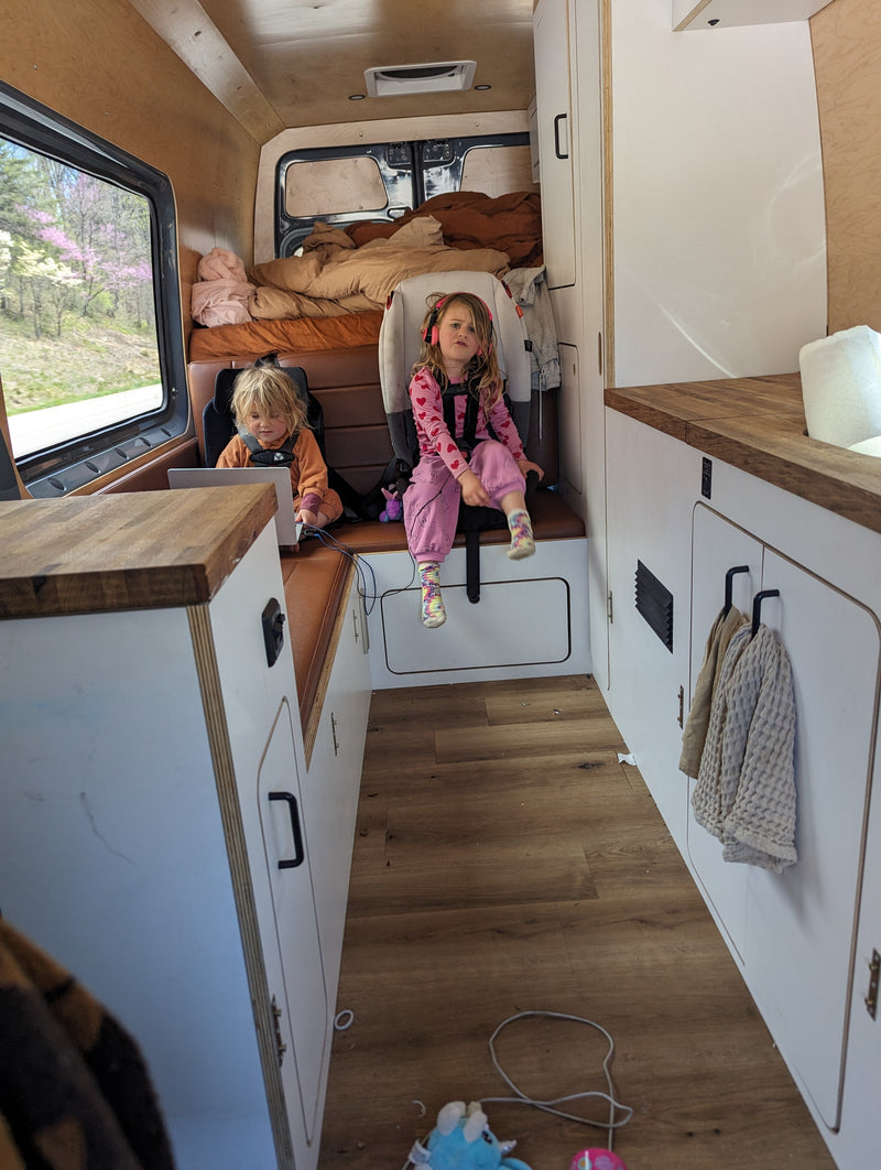 Kids enjoying an RV rental! One uses a laptop, the other wears headphones in this cozy camper van interior with scenic views. — photo 12