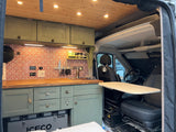 Cozy RV rental kitchen with green cabinets, tiled backsplash, and wooden ceiling. Front seat swivels for a dining table.