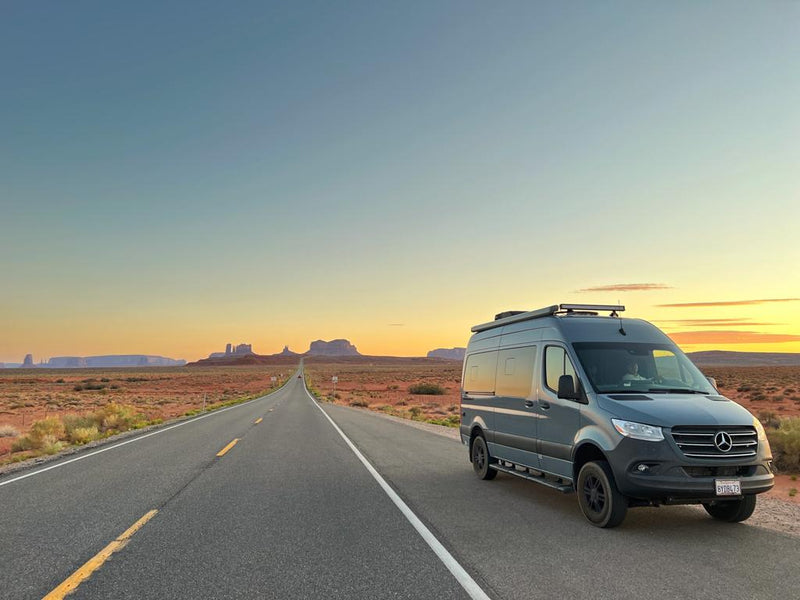  facing Monument Valley's red rock formations at sunset.|Scenic RV rental road trip: Grey Sprinter van on a desert highway with iconic mesas at a vibrant sunset.|Experience stunning sunsets from your RV rental. Blue camper van parked on a dirt road in a vast — photo 2