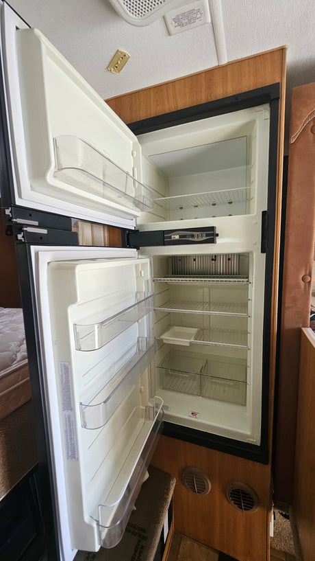 Clean, empty refrigerator and freezer in an RV rental, featuring shelves and clear bins, ready for use.