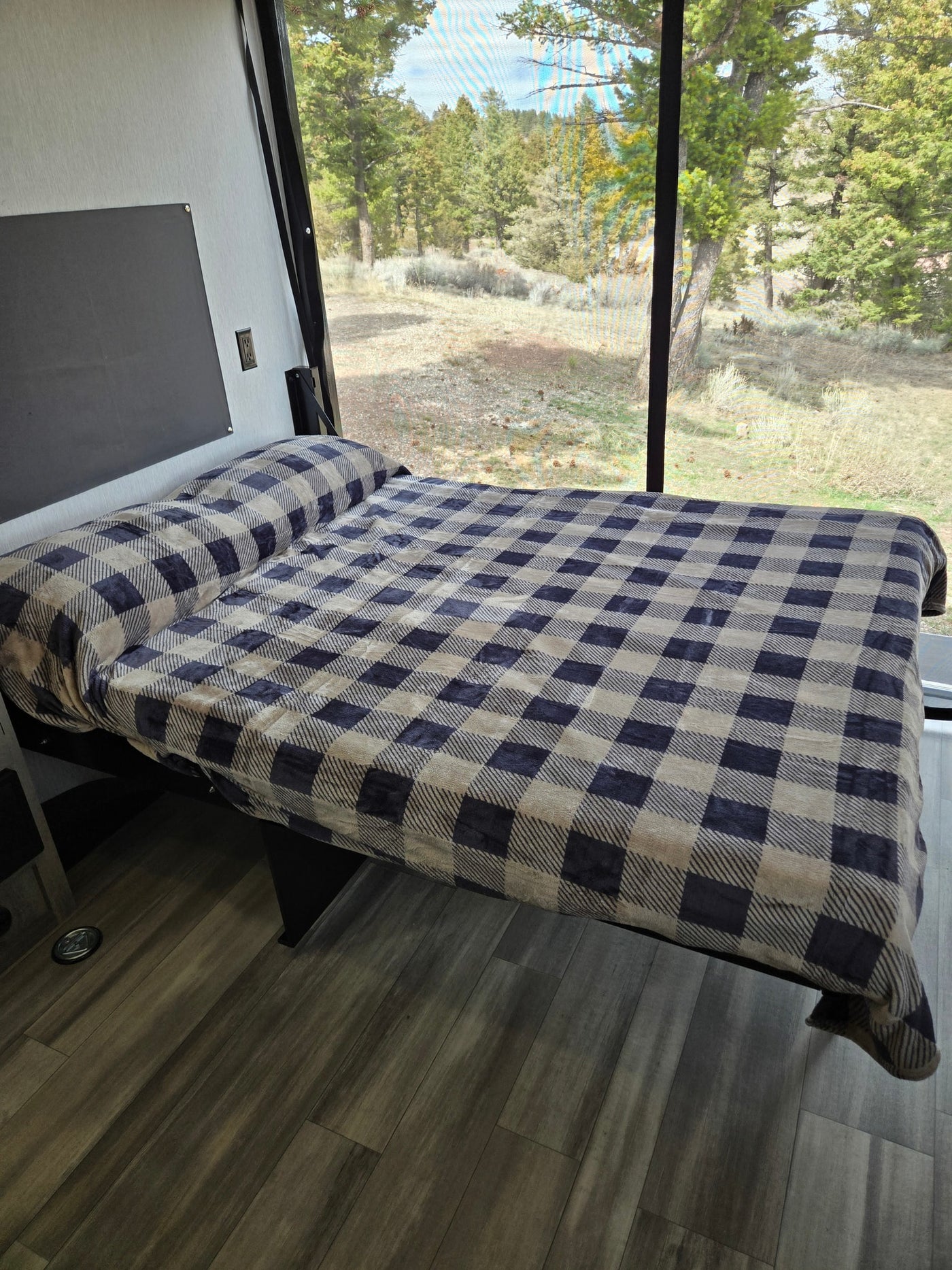  and pine trees overhead.|Compact RV rental interior: pop-out bed with plaid blanket — photo 8