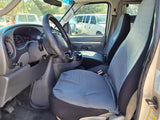 Inside an RV rental van: dashboard, steering wheel, and front seats with patterned covers. Other vans visible outside.