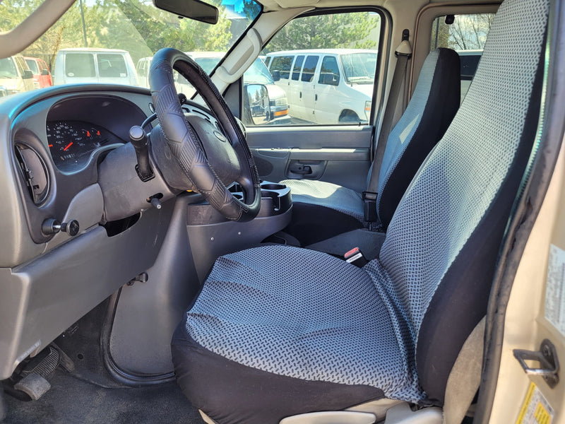 Inside an RV rental van: dashboard, steering wheel, and front seats with patterned covers. Other vans visible outside. — photo 11