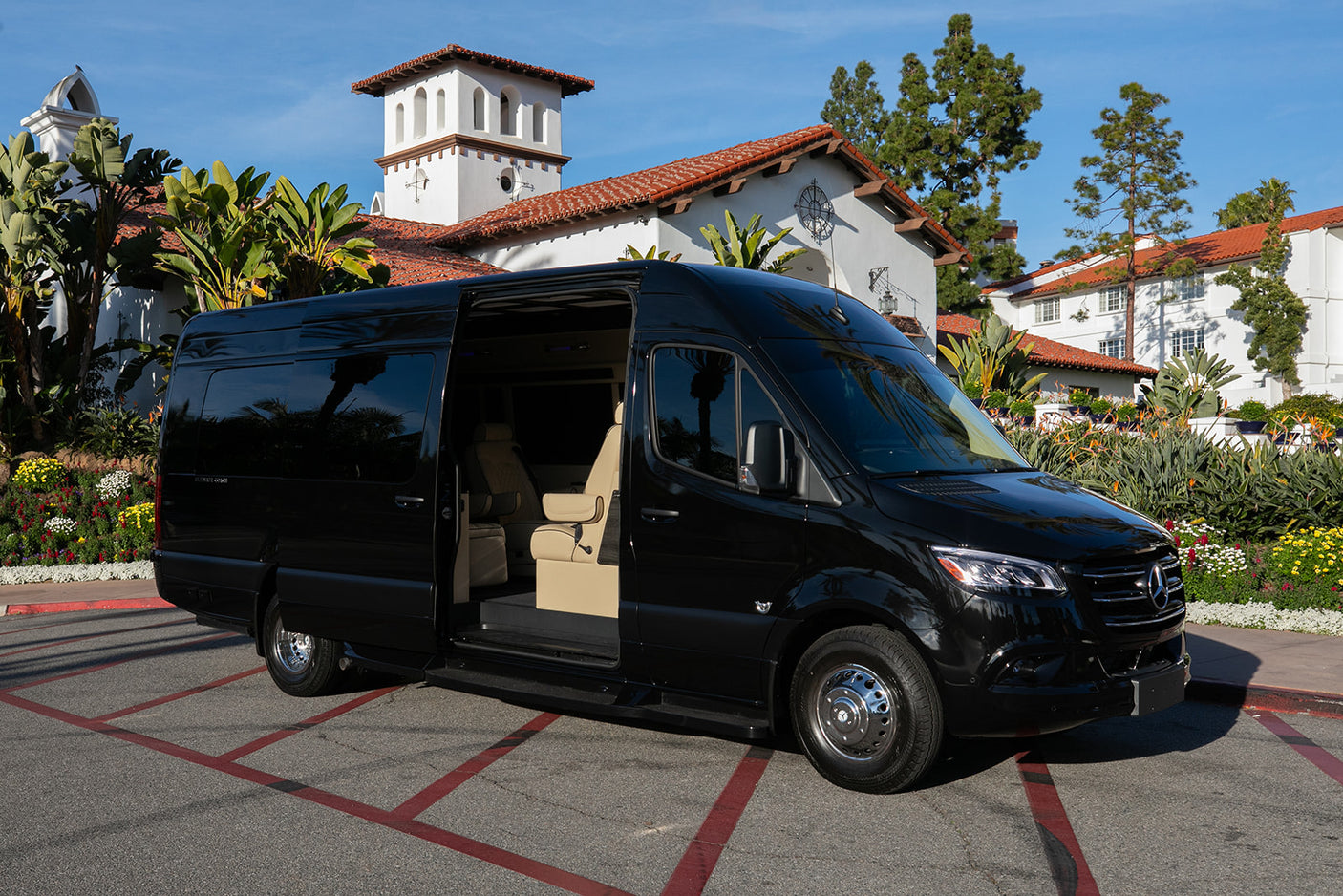 Luxury black Mercedes Sprinter van, an upscale RV rental, parked amidst elegant Spanish architecture and lush gardens.