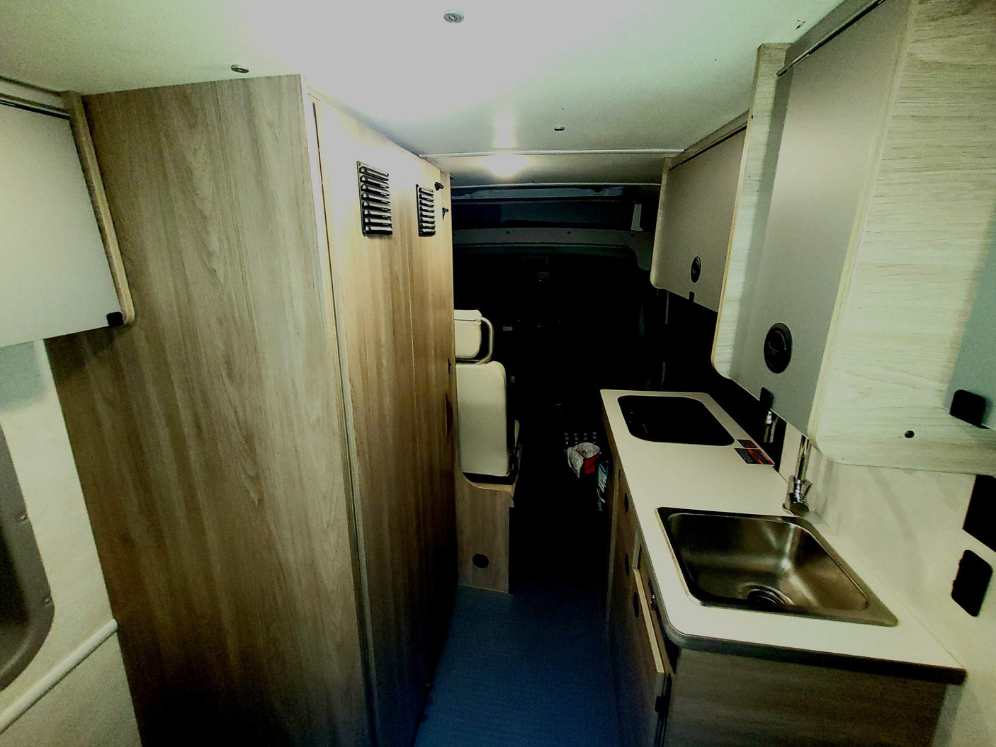 RV rental interior: A bright, modern camper van galley kitchen with a sink, cabinets, and narrow hallway. Perfect for travel.